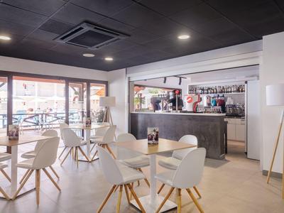 Moderní hotelový bar s bílými židlemi, dřevěnými stoly a lesklým černým pultem pod tmavým stropem.