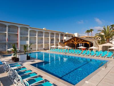 Venkovní hotelový bazén s modrými lehátky a jasnou oblohou.