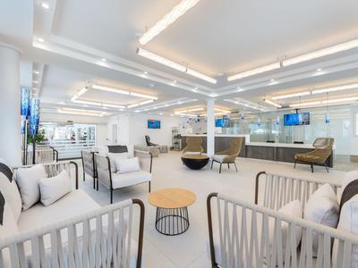 Jasná moderní hotelová hala s bílými stěnami, pohodlnými křesly a dřevěnými stolky pod stropními světly.