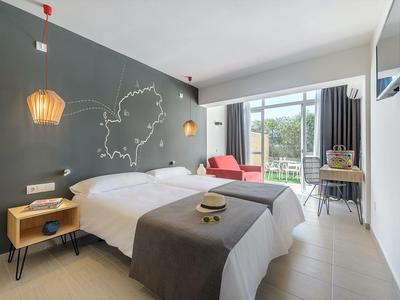 Moderní hotelový pokoj se dvěma lůžky, tmavě šedou zdí a posuvnými dveřmi do zahrady.