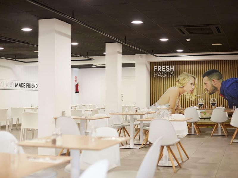 Moderní, prostorná kavárna s dřevěnými stoly, bílými židlemi a žlutou pruhovanou zdí s nástěnnou malbou.