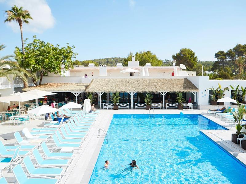 Jasný venkovní bazén vedle bílých lehátek pod slunečníky v slunném letovisku.