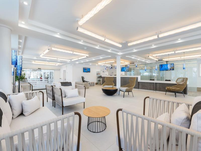Jasná moderní hotelová hala s bílými stěnami, pohodlnými křesly a dřevěnými stolky pod stropními světly.
