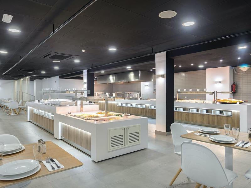 Prostorná moderní bufetová oblast s osvětlenými pulty a pečlivě prostřenými stoly.