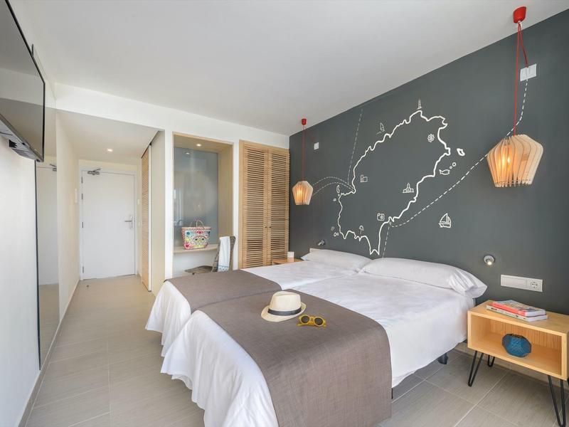 Moderní hotelový pokoj s dvojlůžky, dřevěnými nočními stolky a hvězdnou soustavou na zdi.