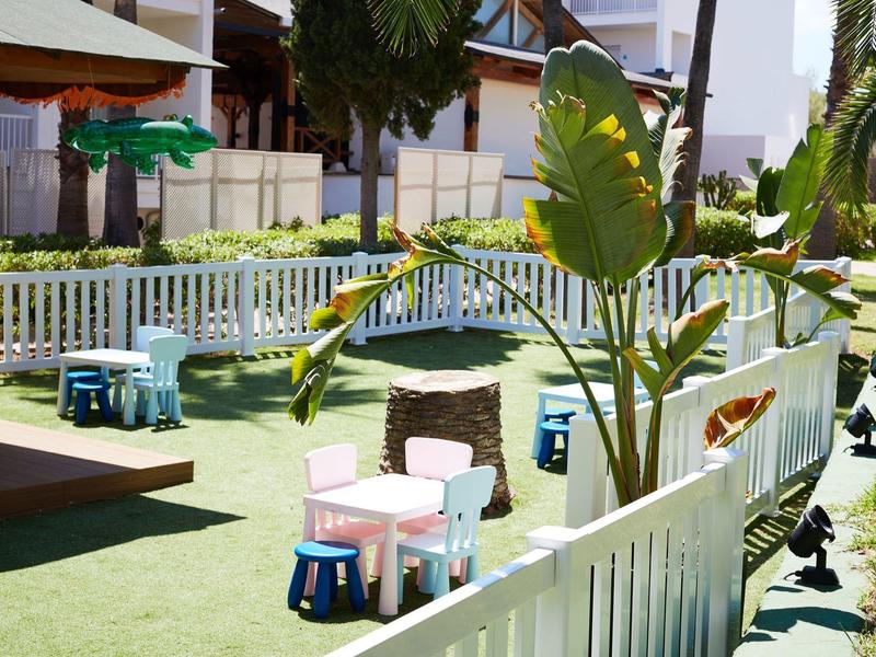 Dětské hřiště s malými stoly a židličkami na trávníku vedle bílého plotu