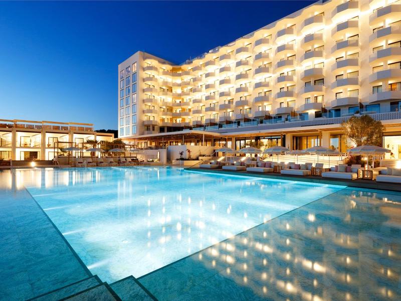 Luxusní hotel se osvětleným venkovním bazénem za soumraku pod jasnou oblohou.