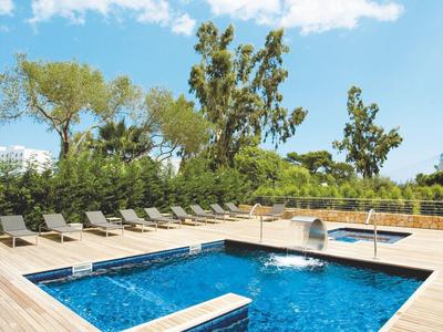 Moderner, rechteckiger Pool mit Holzdeck, umgeben von Liegestühlen und Bäumen unter blauem Himmel.