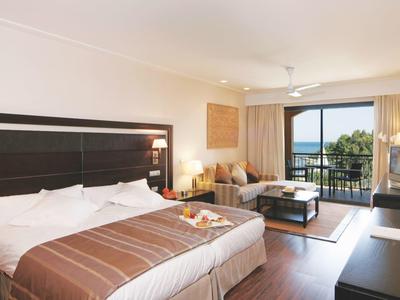 Chambre d'hôtel moderne avec lit double, coin salon et balcon avec vue sur la mer.