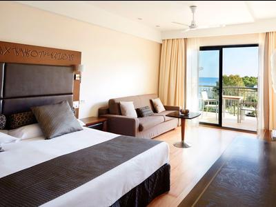 Helles Hotelzimmer mit Doppelbett, Sofa und Balkon mit Meerblick.