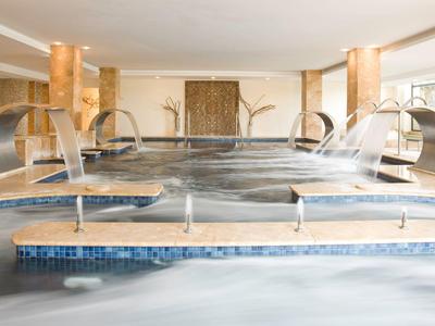 Innenbereich eines modernen Wellnesspools mit mehreren Wasserfällen und dekorativen Säulen.