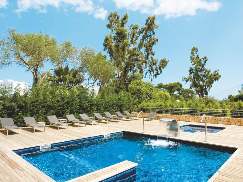 Piscine moderne avec terrasse en bois et chaises longues sous un ciel bleu avec des nuages.