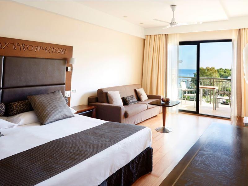 Chambre d'hôtel lumineuse avec lit double, canapé et balcon avec vue sur la mer.