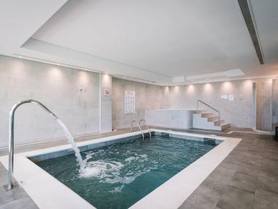 Moderní vnitřní bazén se vodními tryskami a kovovými madly, světlá a relaxační atmosféra.