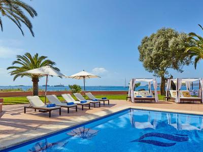 Poolbereich mit Liegestühlen, Sonnenschirmen und Meerblick unter blauem Himmel.