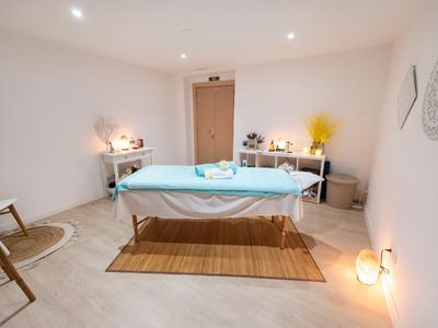 Světle zařízená masážní místnost s lehátkem uprostřed, minimalistický dekor a uklidňující atmosféra.