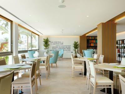 Jasná jídelna s velkými okny, dřevěnými stoly a barevnými židlemi.