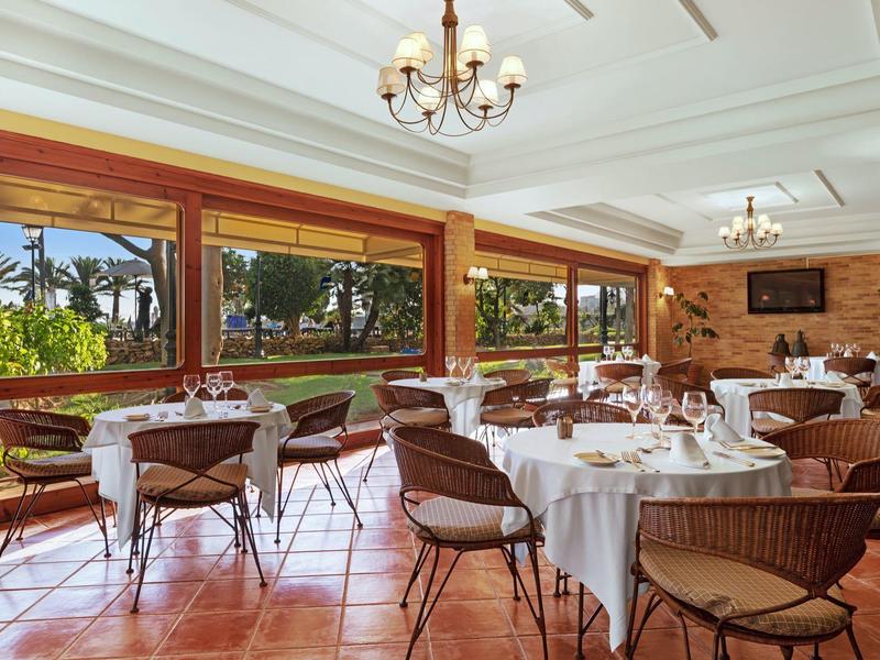 Světlá jídelna s velkými okny a elegantně prostřenými stoly.