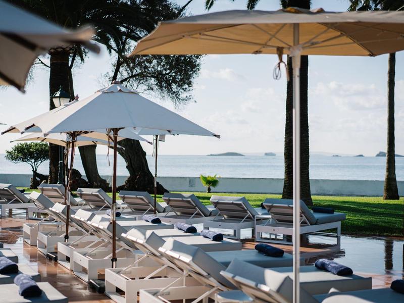 Lehátka pod slunečníky s výhledem na klidné moře a ostrovy na obzoru.