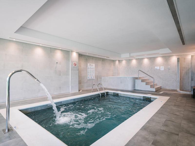 Moderní vnitřní bazén se vodními tryskami a kovovými madly, světlá a relaxační atmosféra.