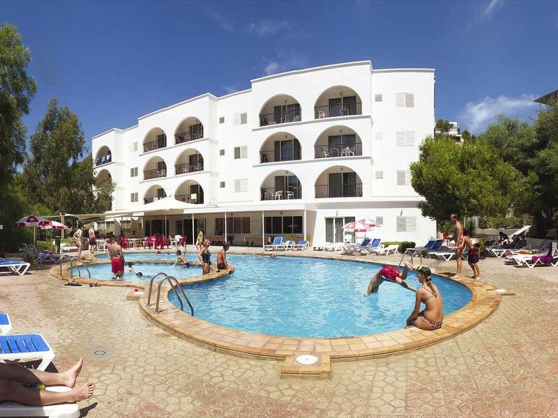 Round swimming pool in front of a white hotel building with multiple balconies and sun loungers.