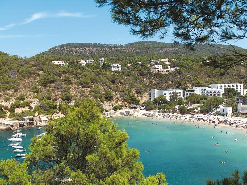 Bay with beach, blue water, surrounding green hills, and hotels.