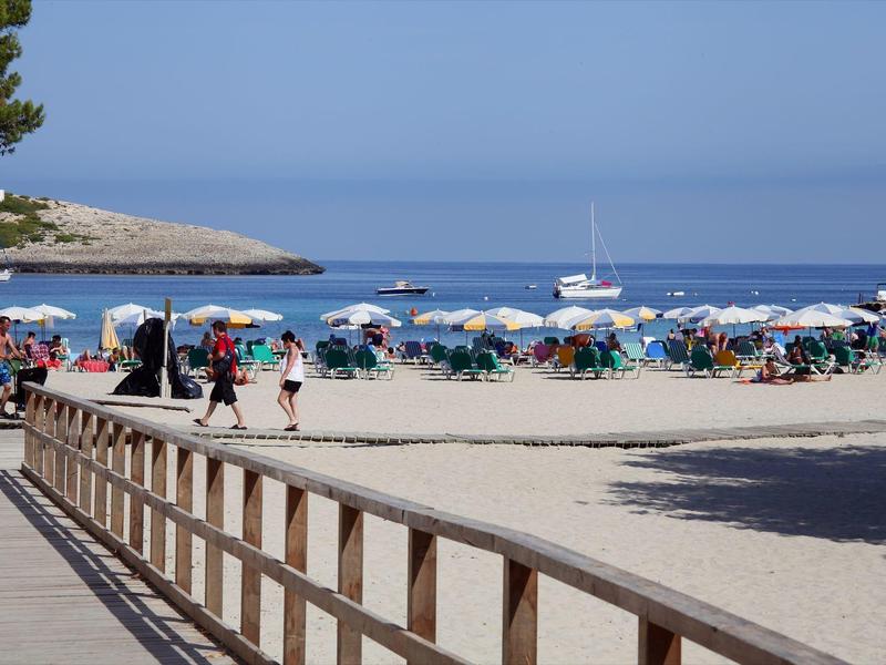 Plage avec parasols, personnes et bateaux sur une mer calme sous un ciel clair