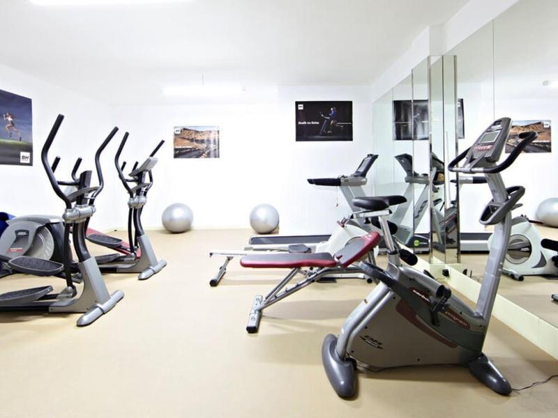 Salle de sport moderne avec divers appareils d'entraînement, miroir mural et ballons de fitness.