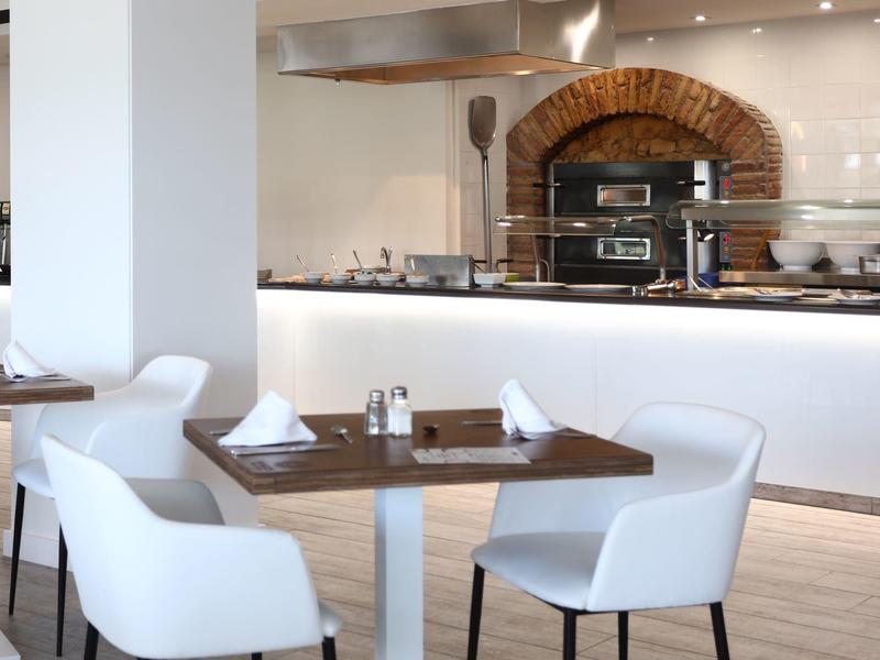 Restaurant moderne avec chaises blanches et cuisine ouverte avec four en arrière-plan.