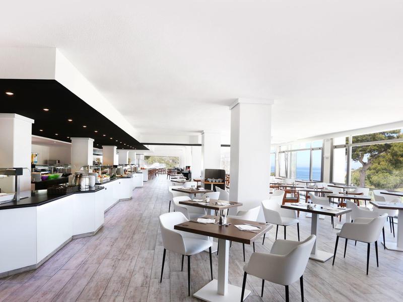 Espace de restaurant moderne et lumineux avec tables, chaises, grandes fenêtres et comptoir en libre-service.