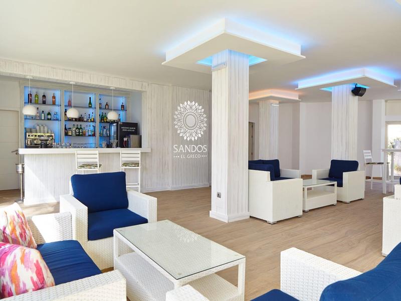 Espace lounge d'hôtel aménagé modernement avec des meubles blancs et des coussins bleus.