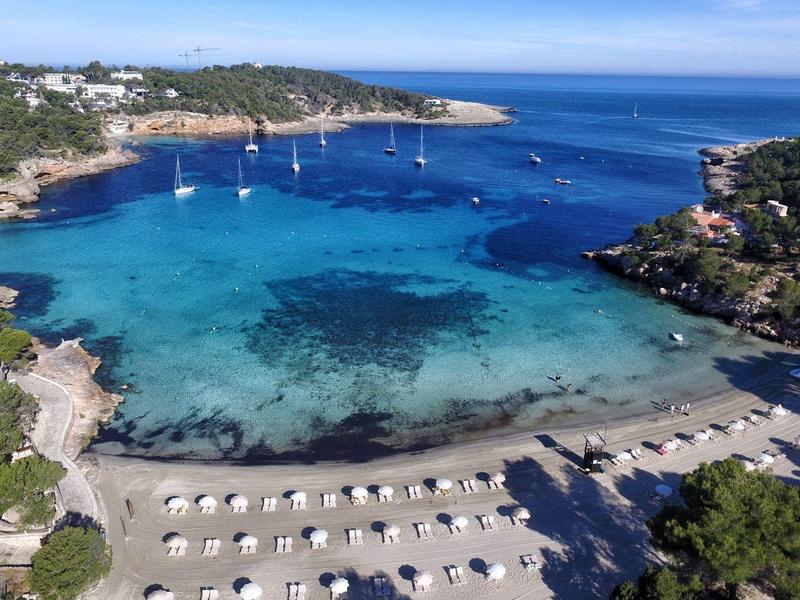 Eaux claires et bleues de la baie avec transats et voiliers dans une station balnéaire.