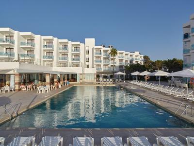 Piscina moderna dell'hotel con lettini, ombrelloni e edificio su più piani sotto un cielo limpido.