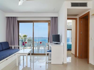 Helles Wohnzimmer mit Sofa, Glastisch und Balkon mit Meerblick in einem Hotelzimmer.