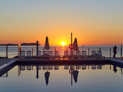 Zachód słońca nad basenem z leżakami i parasolami przy wodzie.