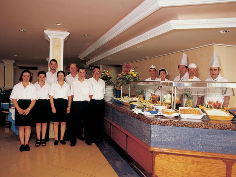 Personel hotelu stoi przy bufecie z różnymi potrawami.