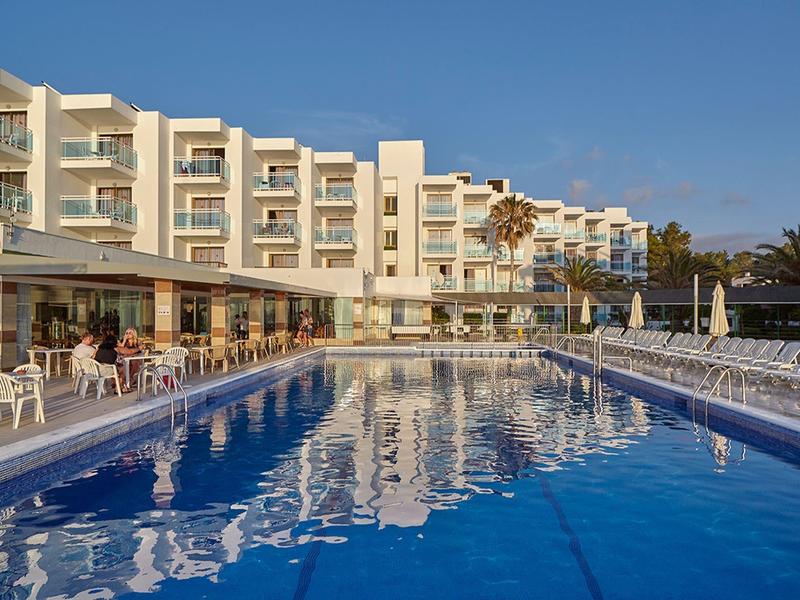 Wielopiętrowy budynek hotelowy obok dużego basenu na zewnątrz z parasolami przeciwsłonecznymi.