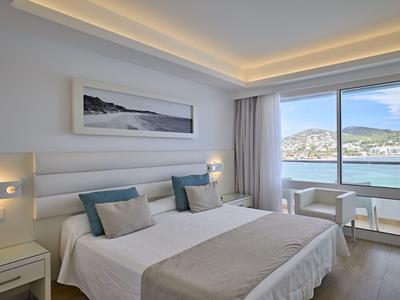 Helles Hotelzimmer mit Doppelbett und großem Fenster mit Meerblick.