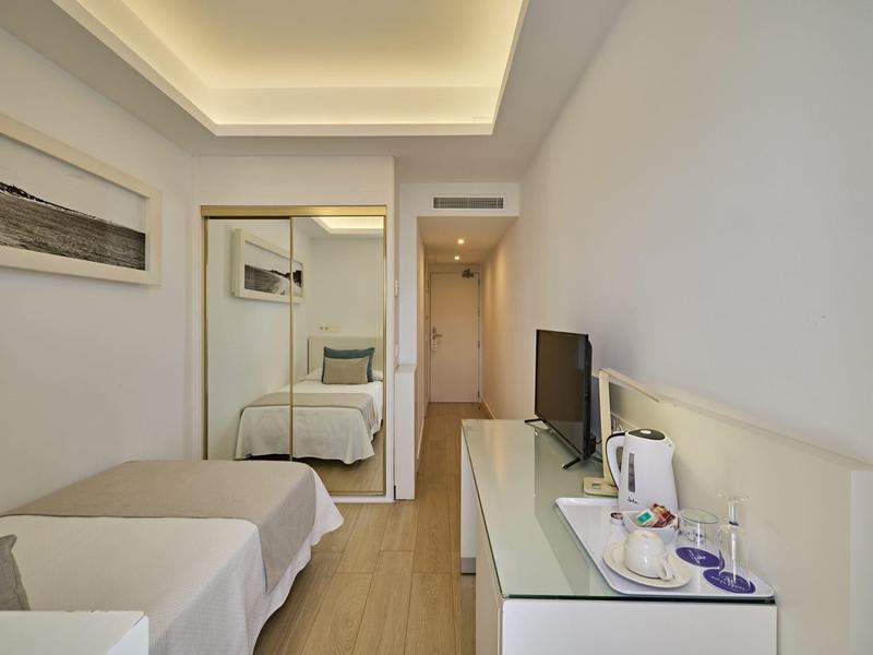 Modern hotel room with bed, mirrored wardrobe, and TV on dresser.