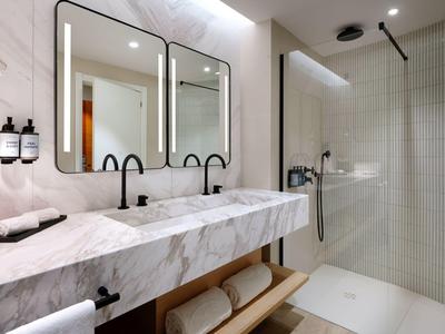 Bagno elegante con doppio lavabo in marmo e doccia a filo pavimento moderna.