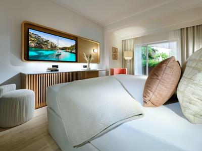 Camera d'hotel moderna con letto comodo, TV a schermo grande e vista sulla vegetazione.