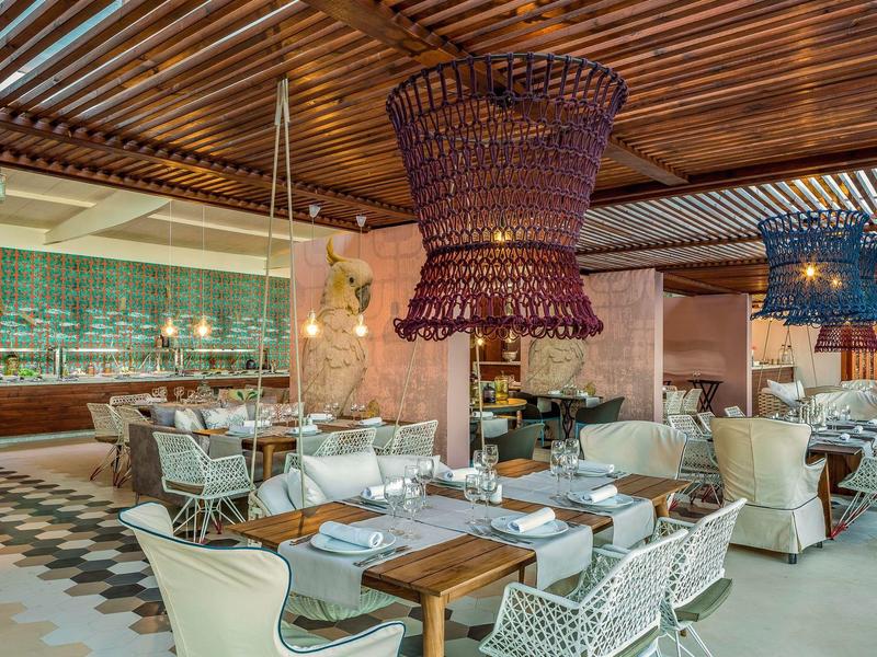 Ristorante elegante con tavoli in legno, sedie bianche, lampade in vimini e soffitto in legno.