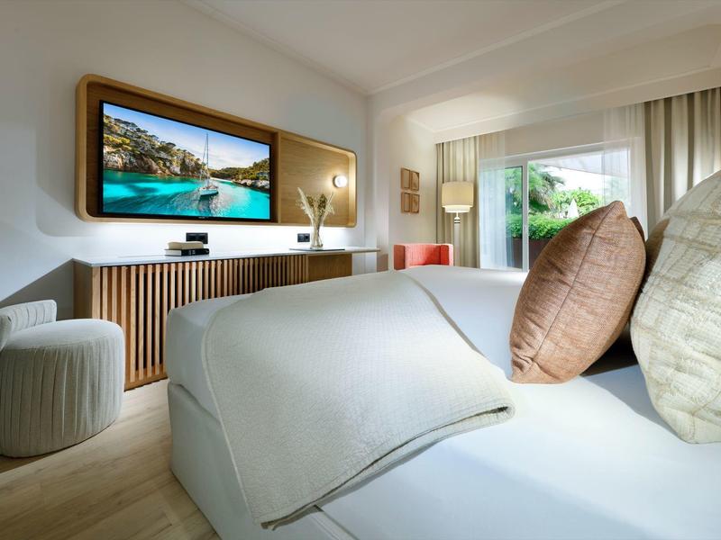 Camera d'hotel moderna con letto comodo, TV a schermo grande e vista sulla vegetazione.