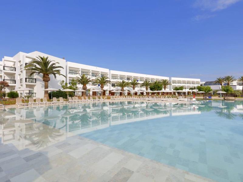 Grande hotel con piscina, palme e cielo sereno.