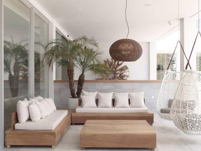 Moderní lounge s bílými polštáři, dřevěným nábytkem a závěsným křeslem v světlé místnosti.