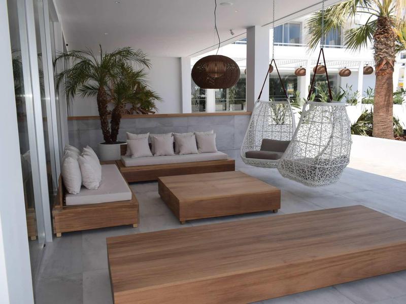 Modern terrace with wooden loungers, hanging chairs, and palm trees for relaxed vacation moments.