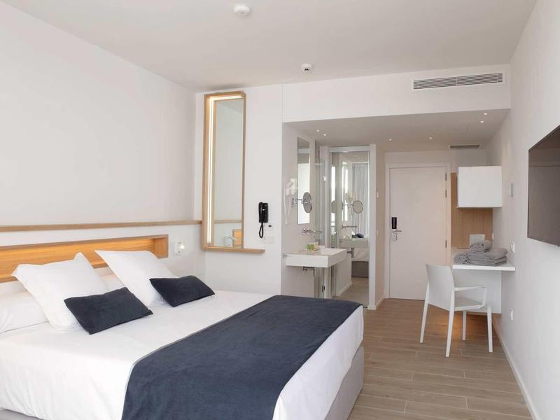 Modern hotel room with double bed, desk, and open bathroom area.