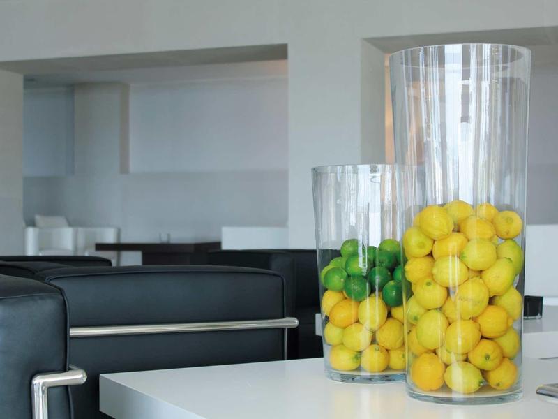 Gläserne Vasen mit Zitronen und Limetten auf weißem Tisch in modernem, minimalistischem Raum.