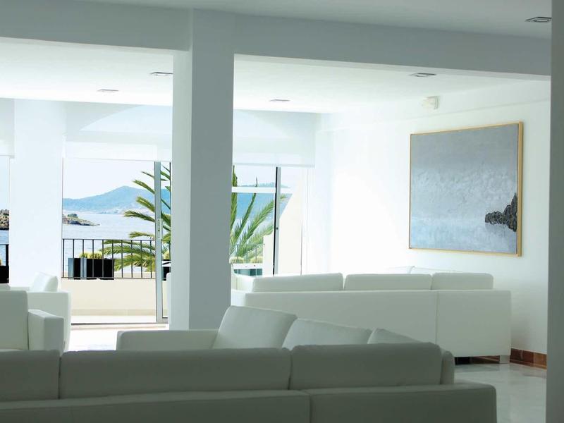 Heller, moderner Wohnraum mit weißen Möbeln, großen Fenstern und Meerblick im Hintergrund.