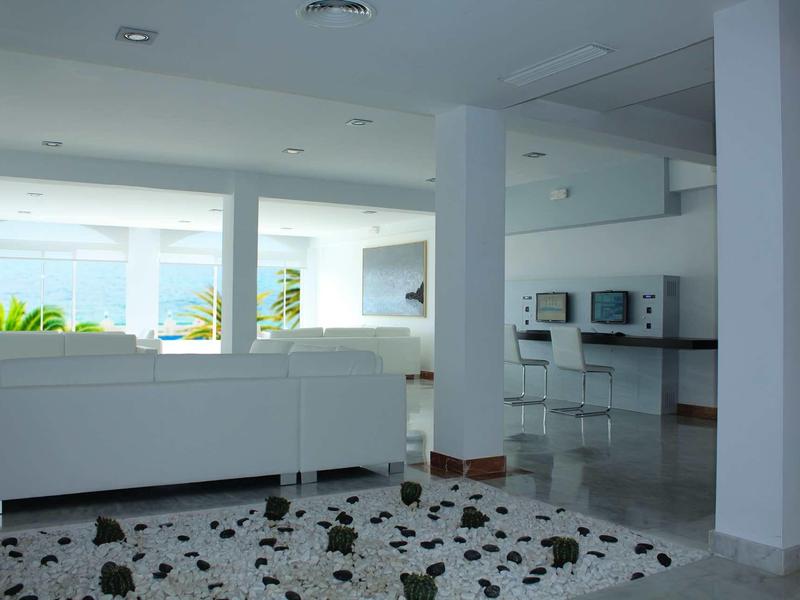 Helles, modernes Wohnzimmer mit weißen Möbeln und Teppich mit schwarzem Muster.